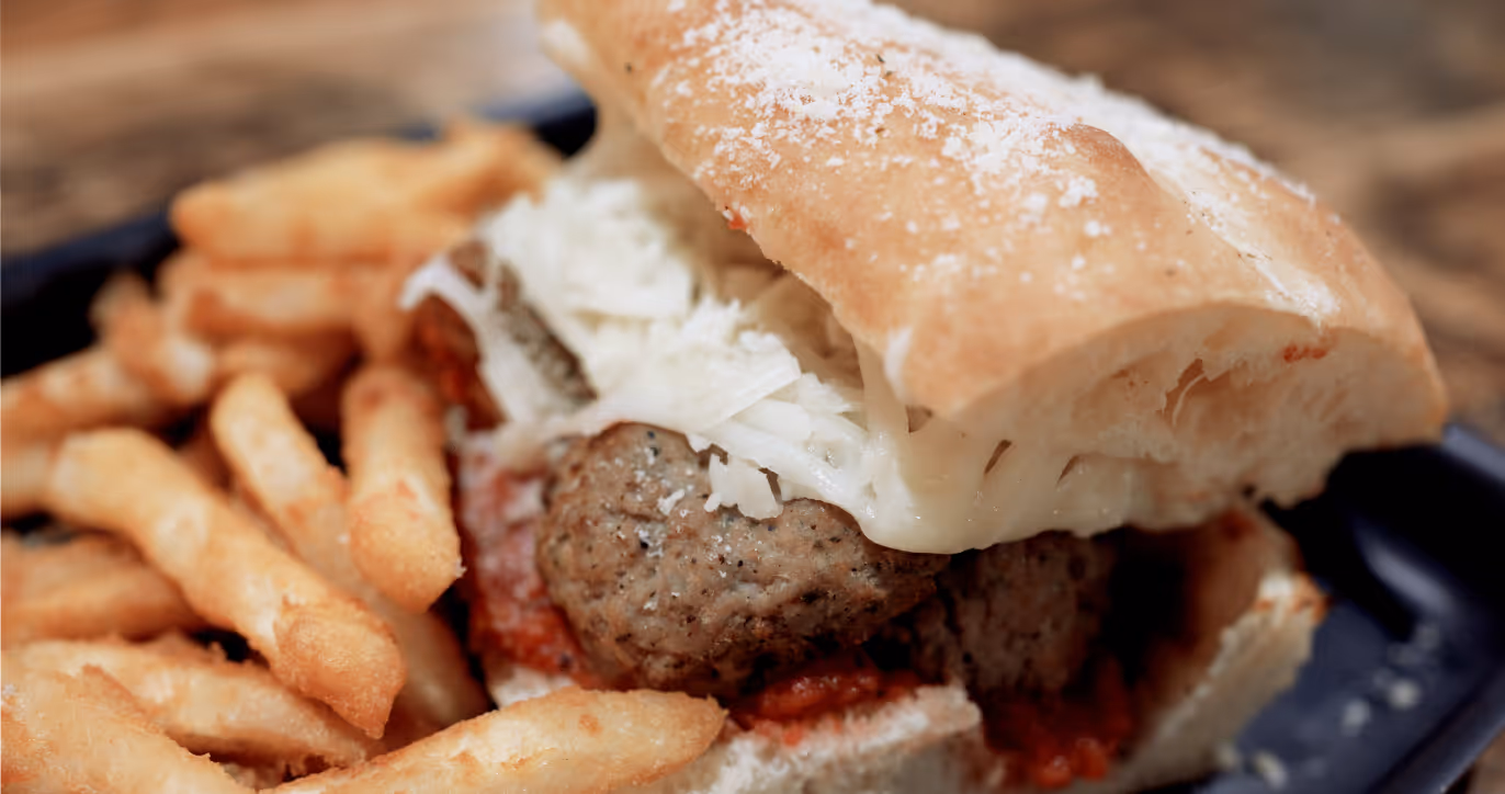 Close-up of a meatball sandwich with parmesan sauce served with fries.