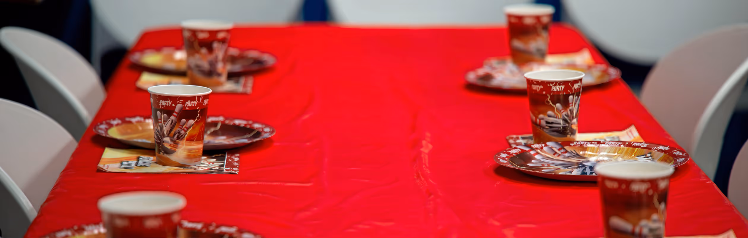 Table decorated with red table cloth and plates, cups and napkins for birthday party.