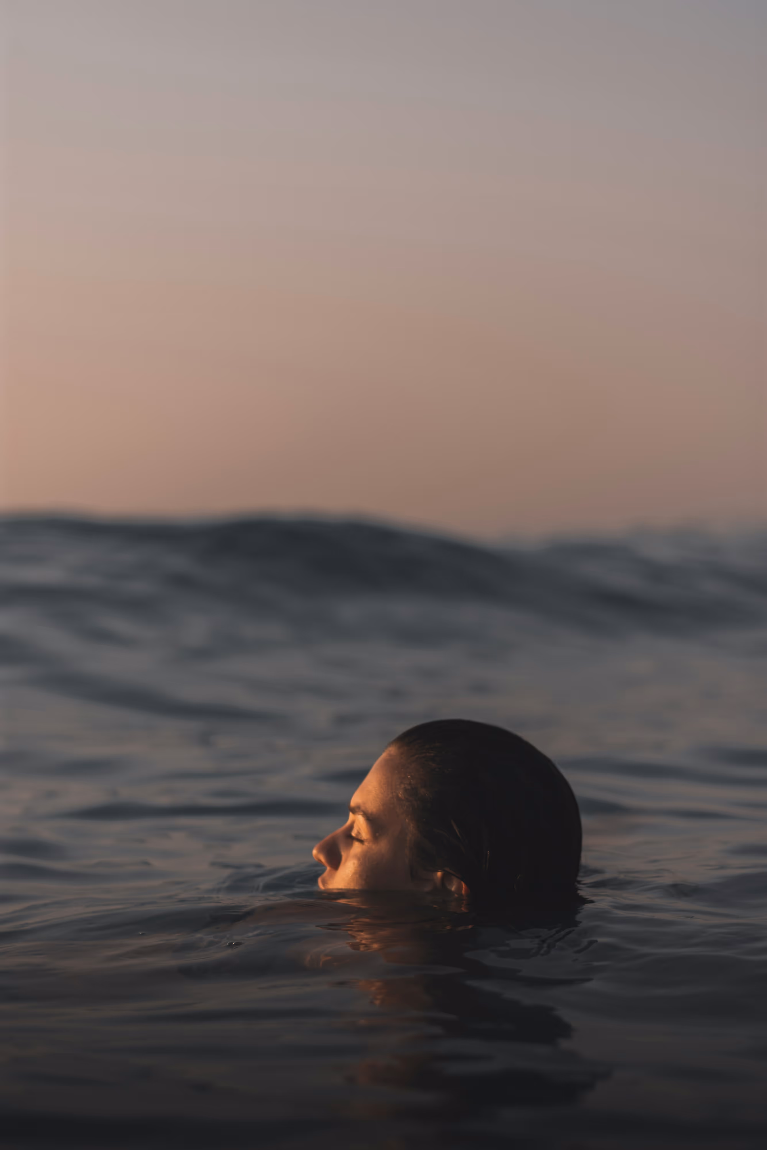 Person with closed eyes immersed in calm ocean water at sunset.