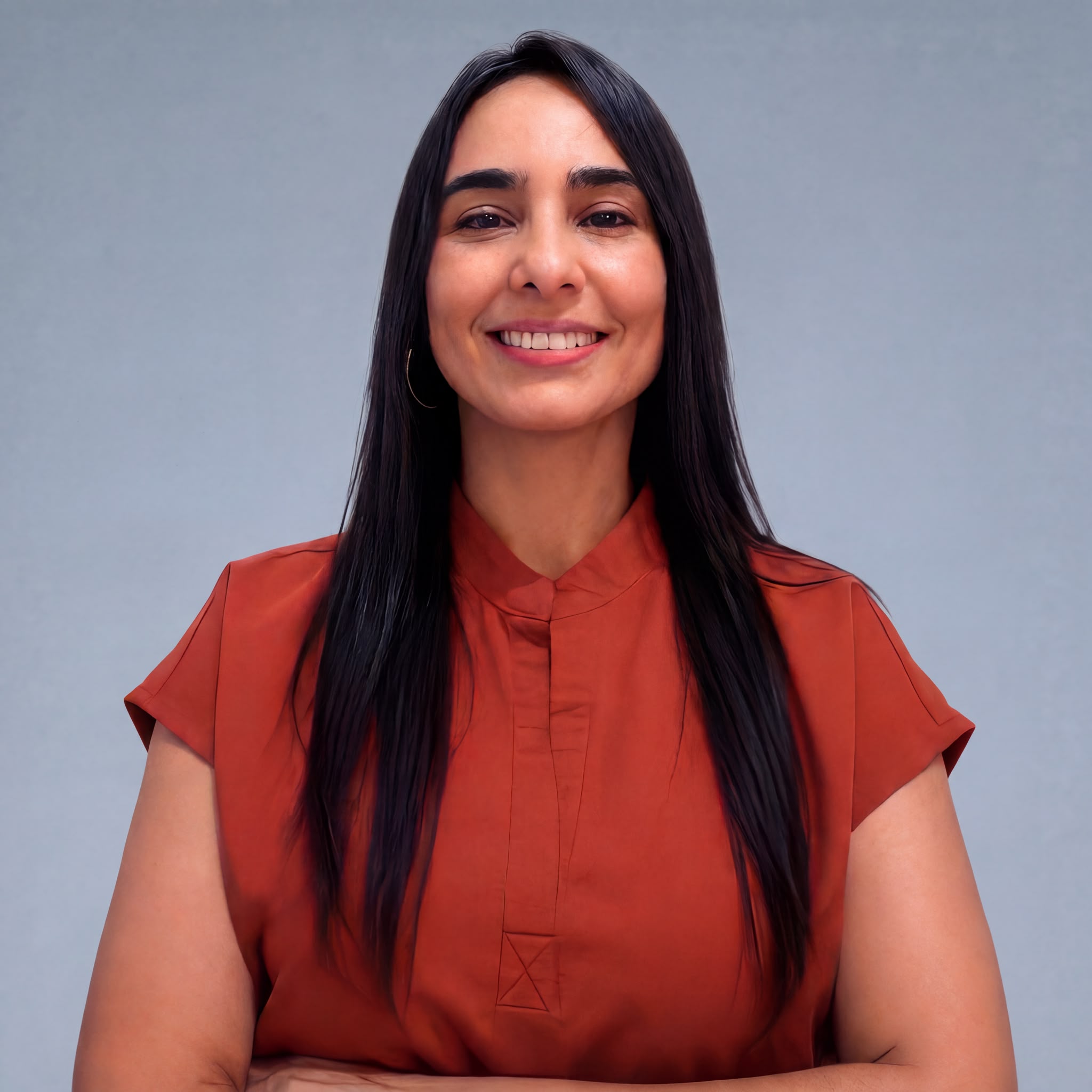 Smiling woman with long black hair wearing rust-colored blouse against gray background.