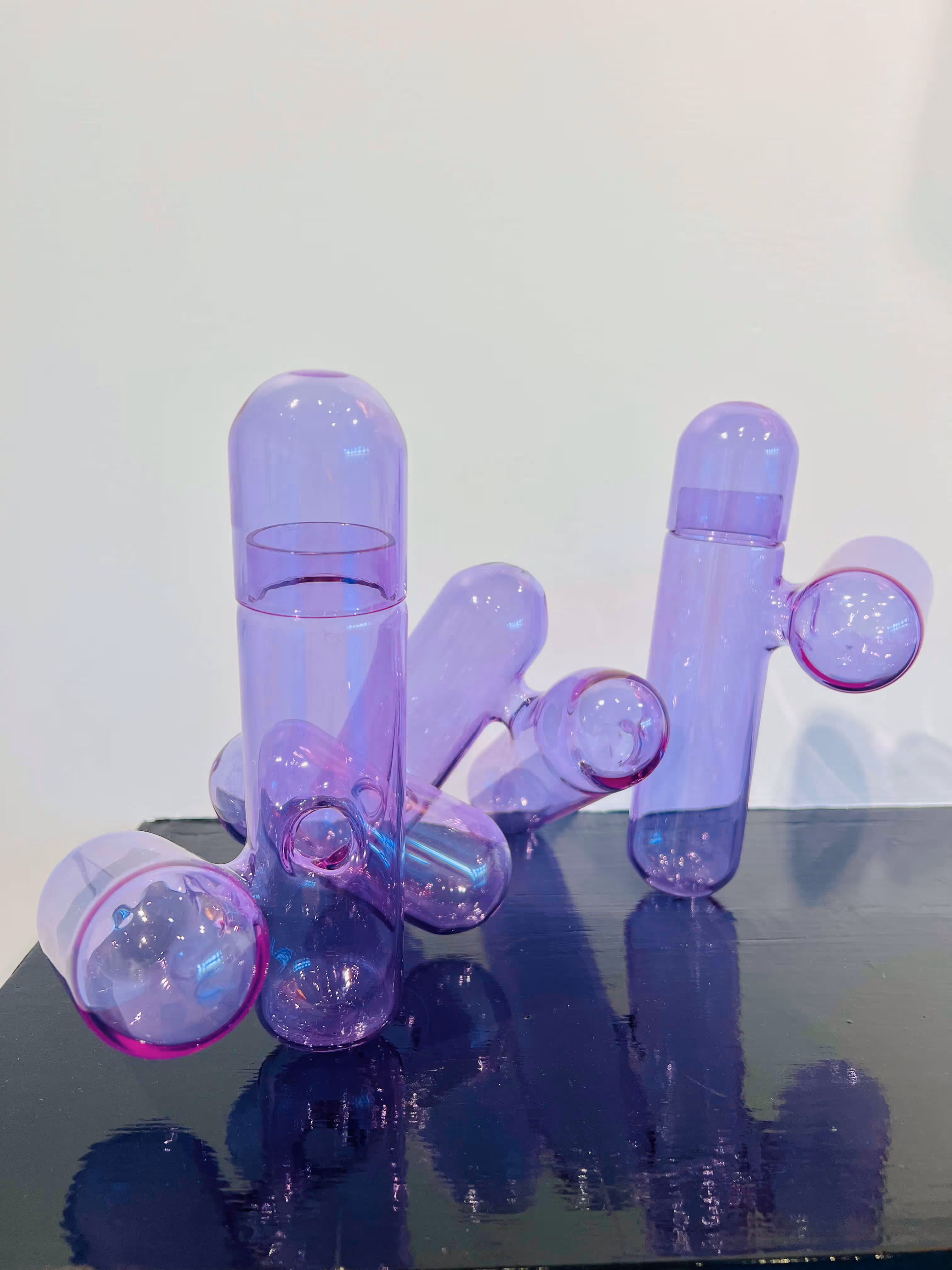 Two abstract purple glass sculptures shaped like capsules with protruding spheres, resting on a reflective black surface.