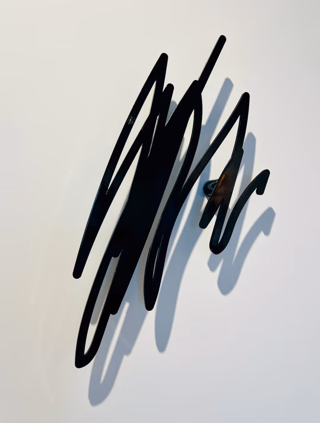 Abstract black metal wall sculpture casting shadow on a white wall.