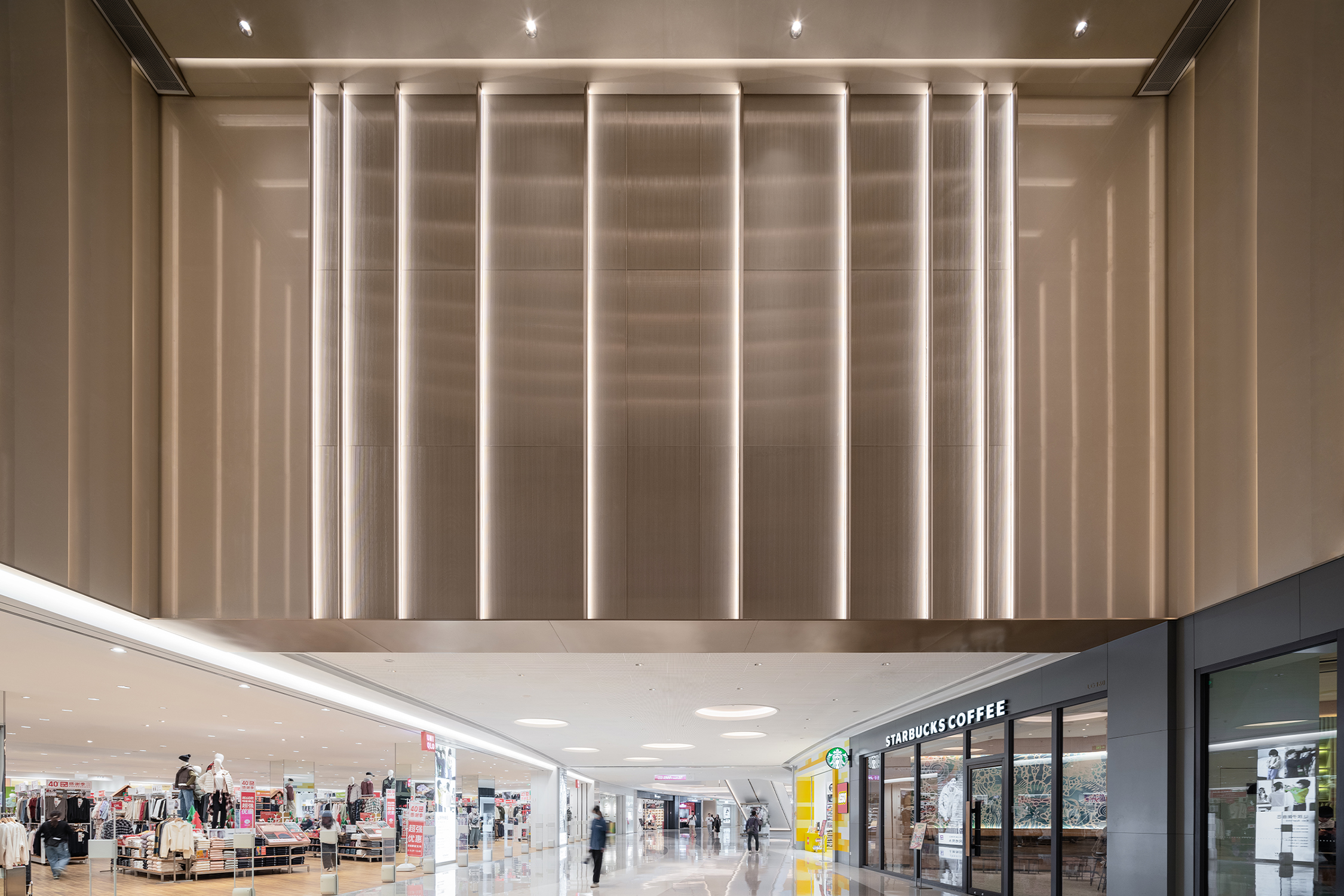 购物中心内现代圆形天花板，中央区域有三角形镜面装饰，周围环绕暖色灯光。