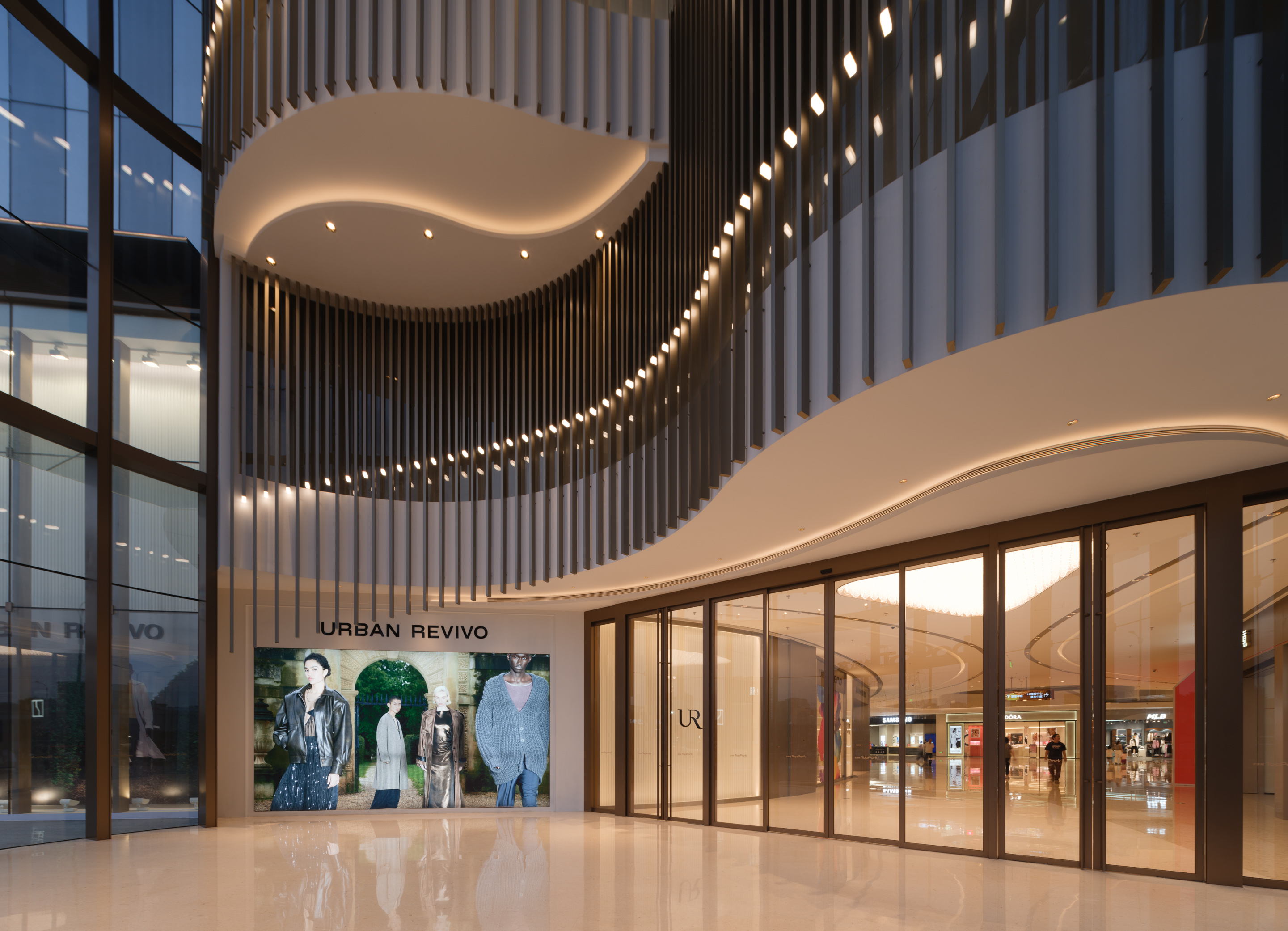 购物中心内现代圆形天花板，中央区域有三角形镜面装饰，周围环绕暖色灯光。