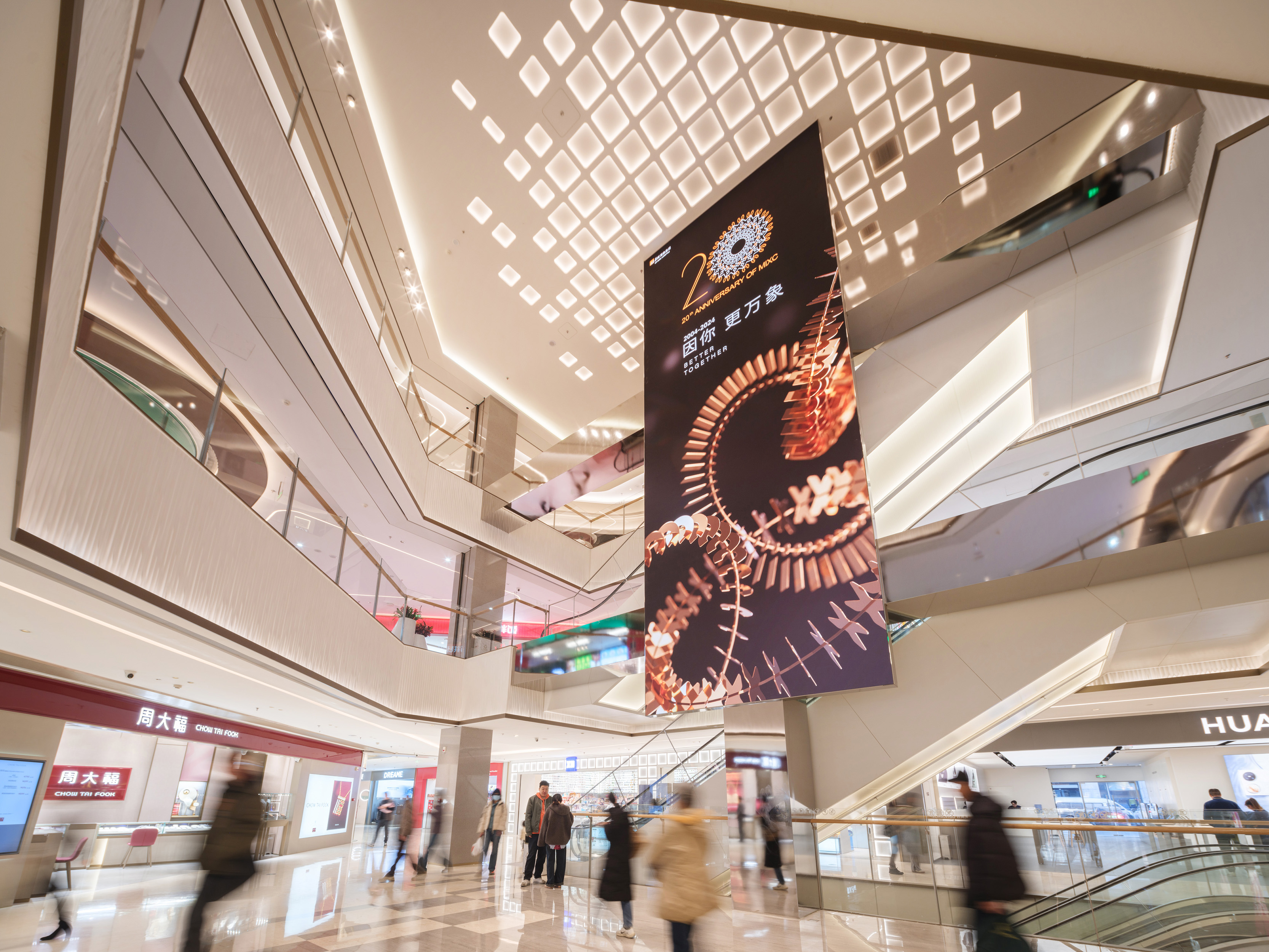 现代购物中心内部，中央有大型玻璃穹顶和多层环绕商铺，右侧有自动扶梯。