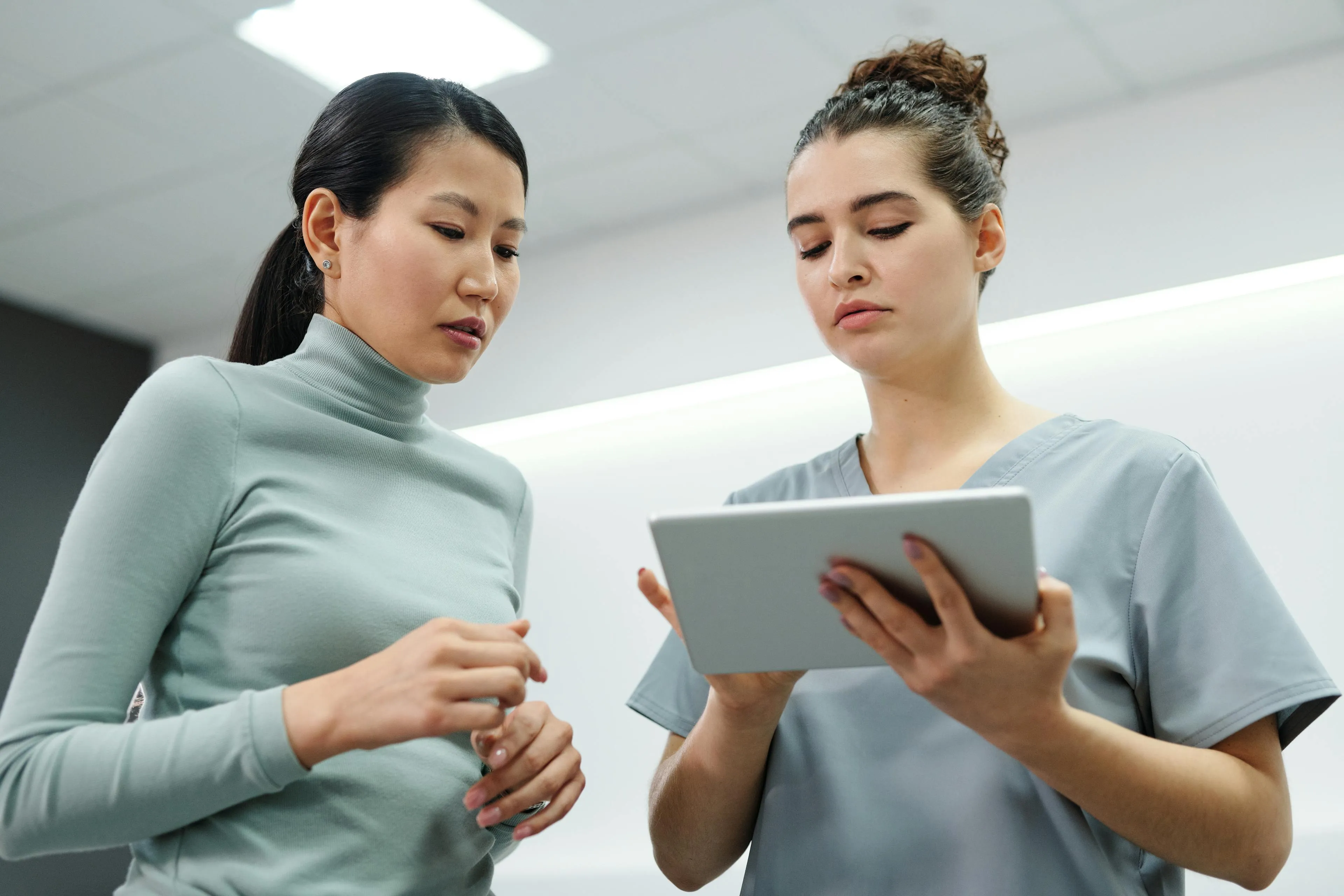 Two women discussing information on a digital tablet in a modern office setting.
