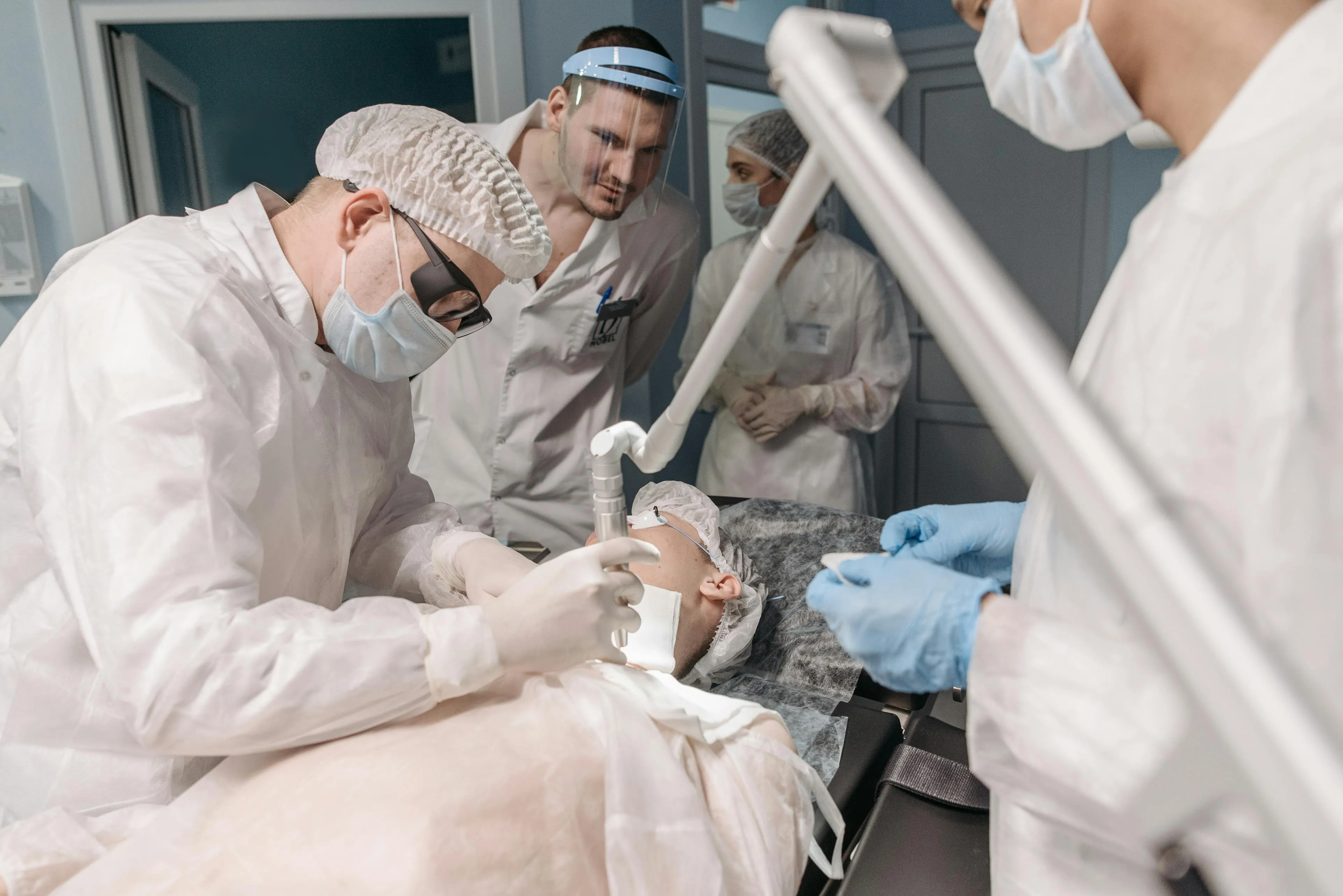 Medical professionals in protective clothing performing a laser treatment on a patient's neck in a clinical setting.
