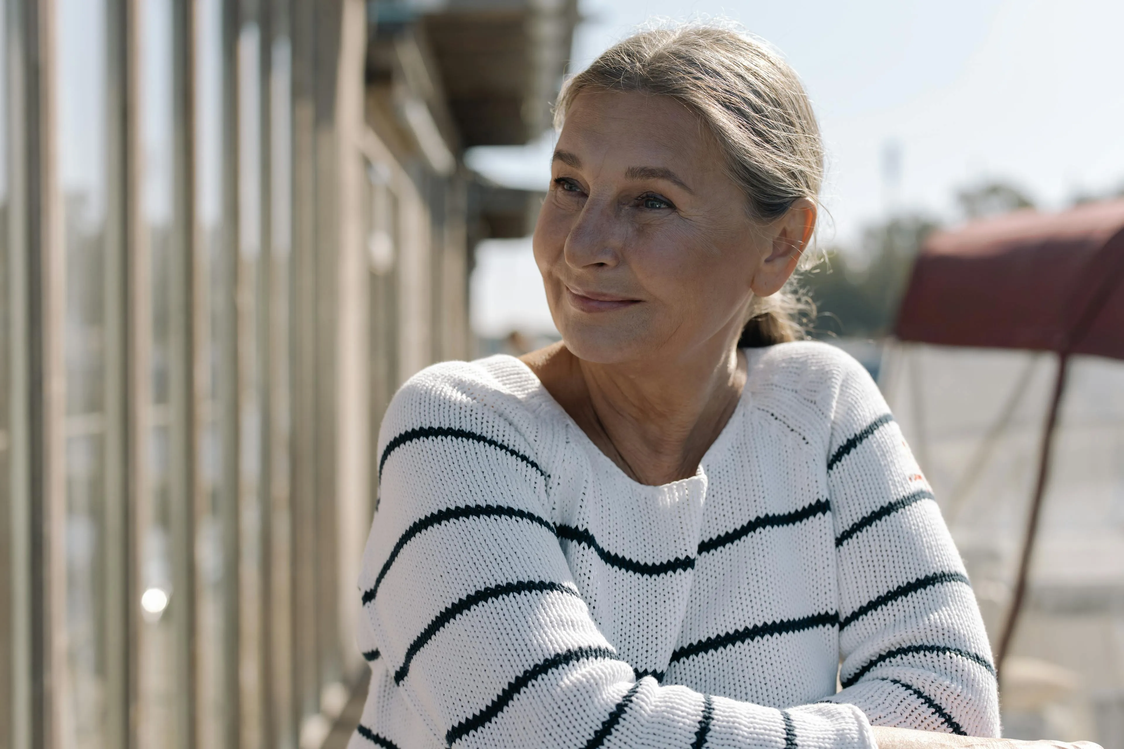 Smiling middle-aged woman wearing a white sweater with black stripes sitting outdoors with arms crossed.