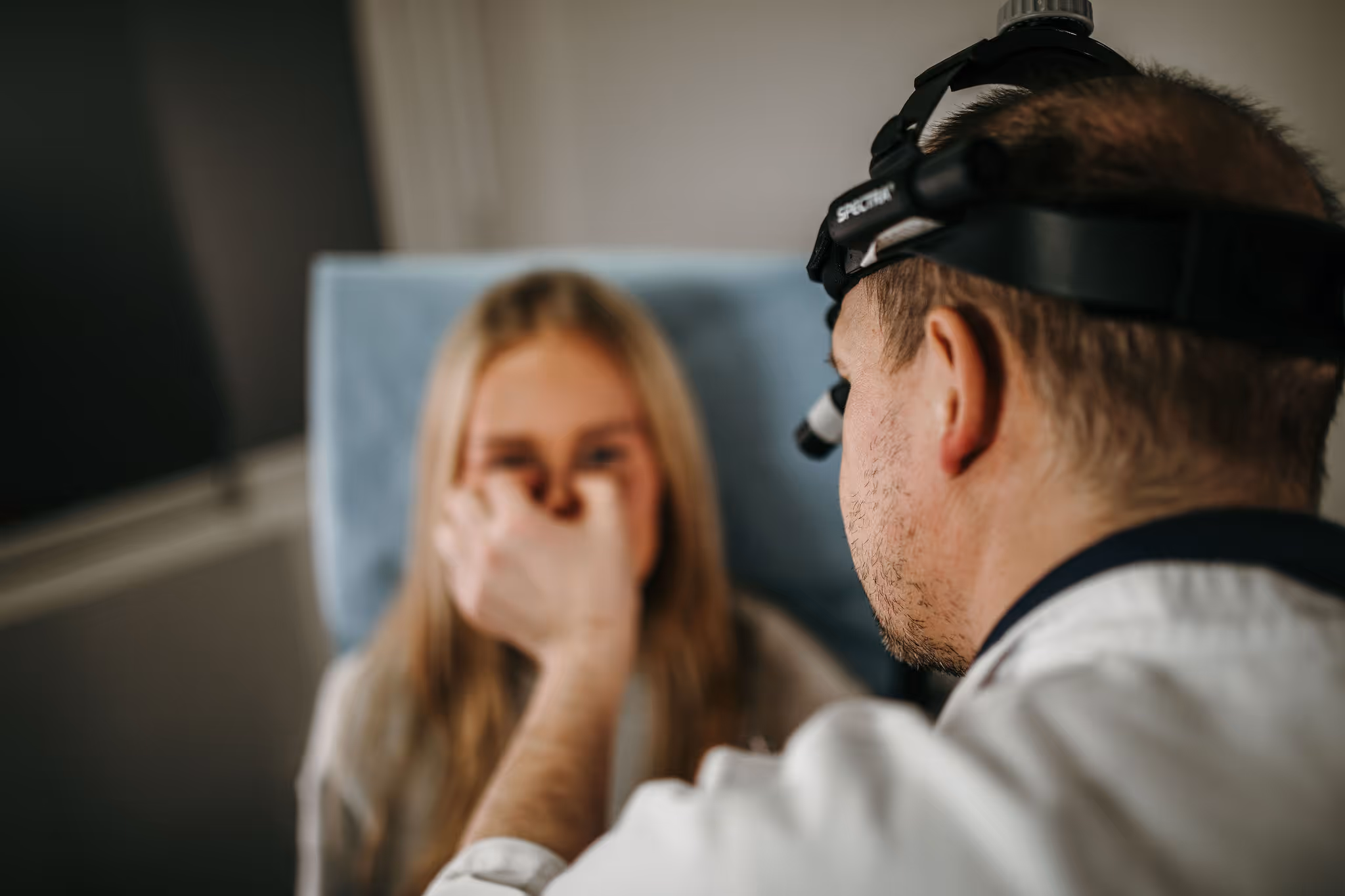 Lege undersøker en ung kvinnes øyne med et hodelys i en klinikk.