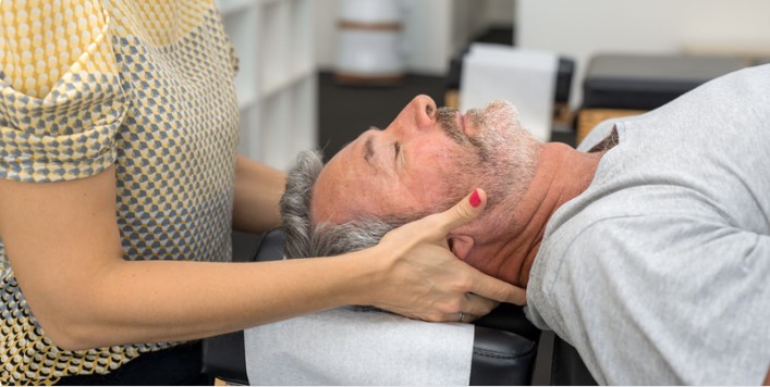 Chiropractor supporting an older man’s head and neck while he reclines on a treatment table
