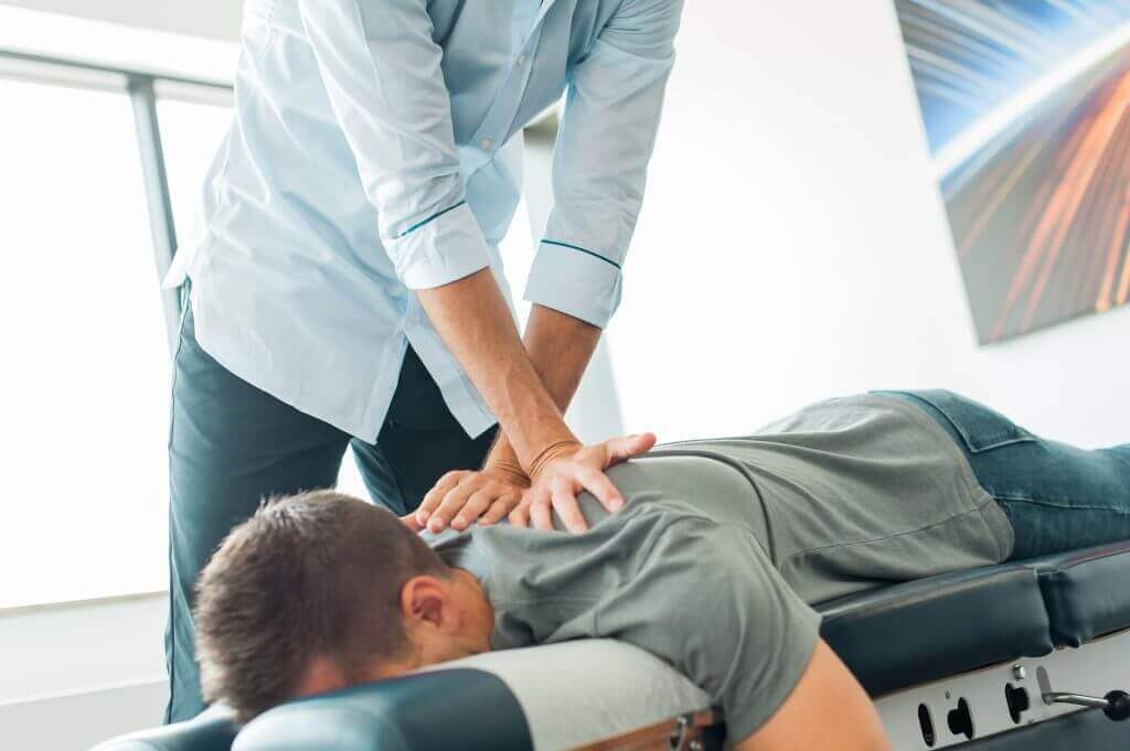 Chiropractor applying pressure to a person's upper back while they lie face down on a treatment table