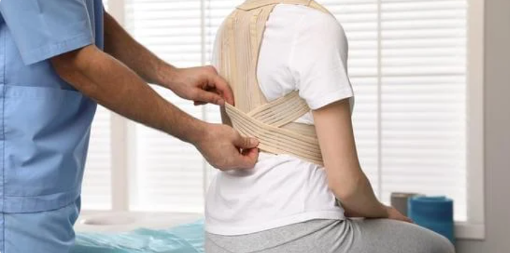 Person fitting a beige posture support brace around another person's upper back and shoulders.