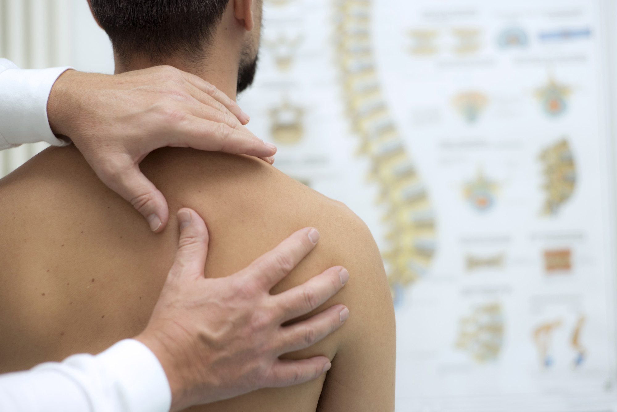 Practitioner’s hands examine a person’s upper back and shoulder.