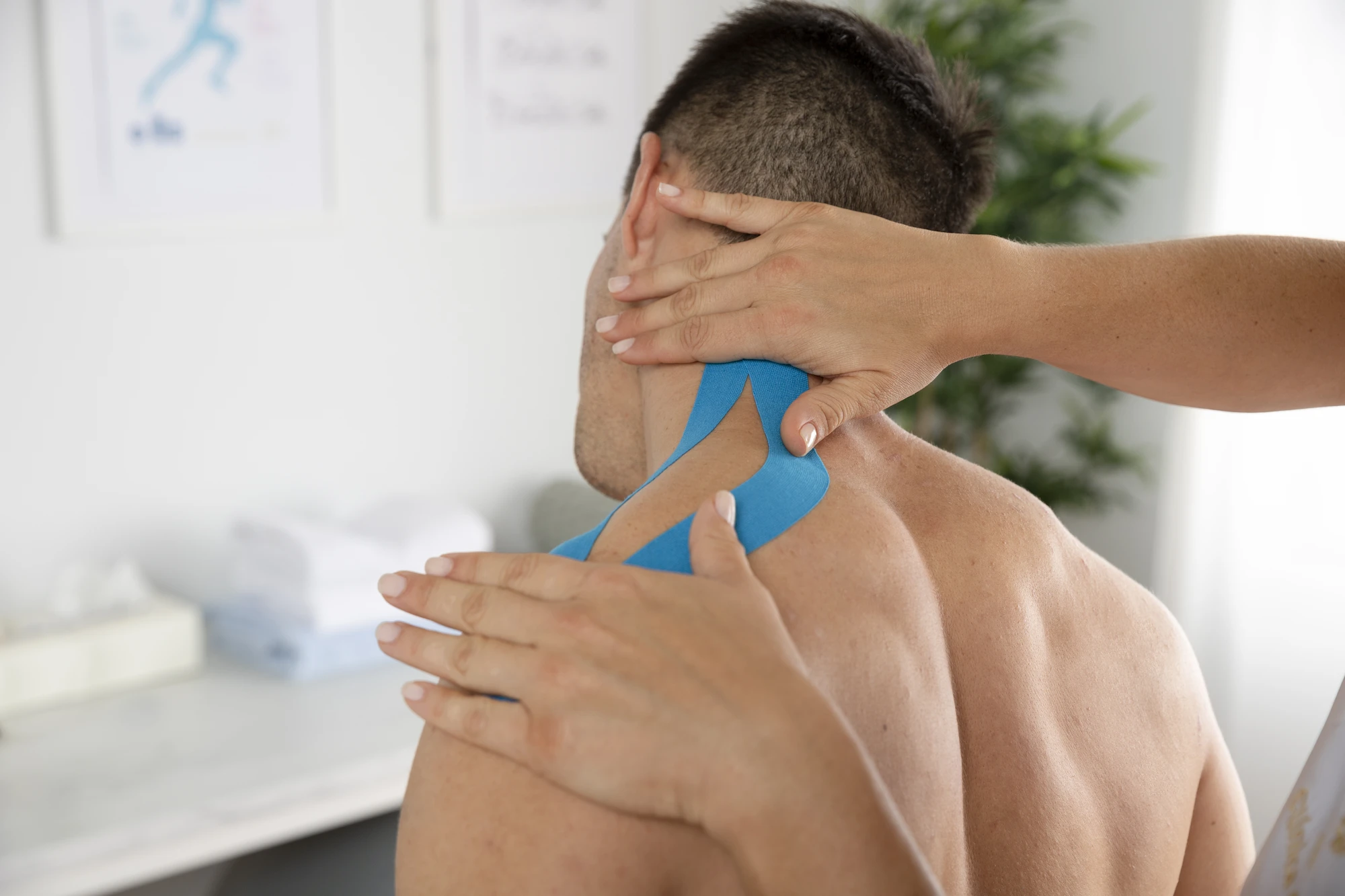Person receiving blue kinesiology tape on the neck and upper shoulder.