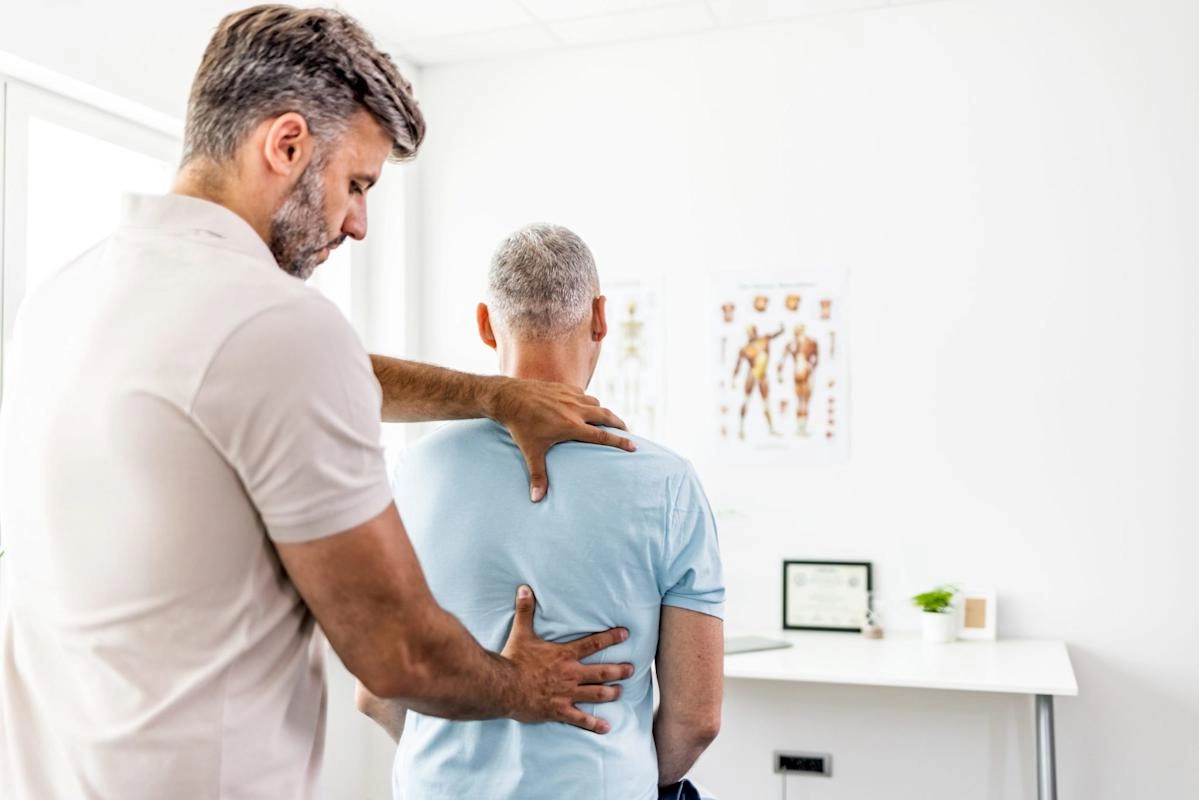 Practitioner gently places hands on an older patient’s upper back and side in a clinical office.