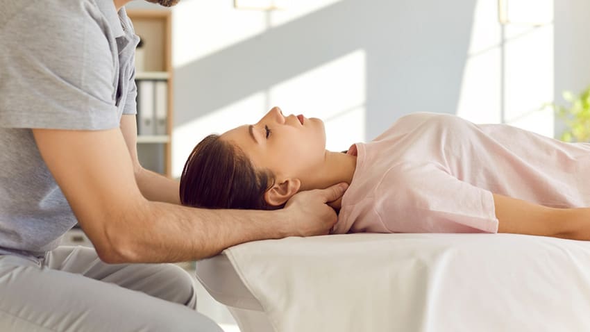 Practitioner supports a woman’s neck as she lies on a treatment table.