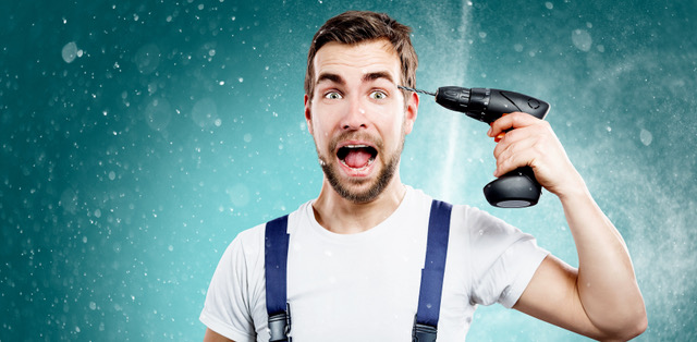 Startled man in work clothes holding a power drill near his ear