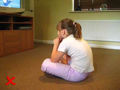 Child sitting cross-legged on the floor watching television, with a red X symbol in the corner