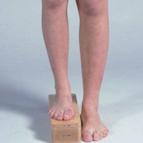 Person standing with one foot on a wooden block, creating an apparent difference in leg length.