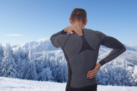 Person in a dark athletic shirt stretching their back against a snowy mountain landscape.