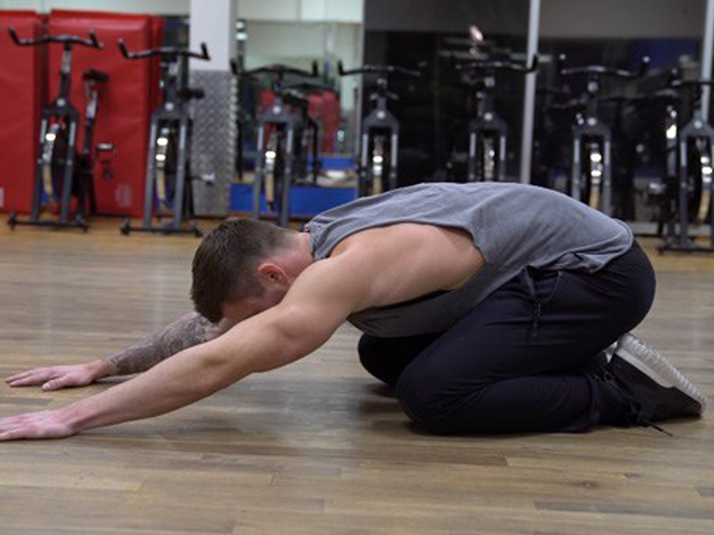 Person kneeling with arms extended forward in a gym stretch.