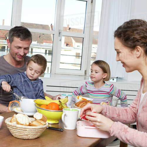 Family eating breakfast together at a kitchen table with two children and two adults.