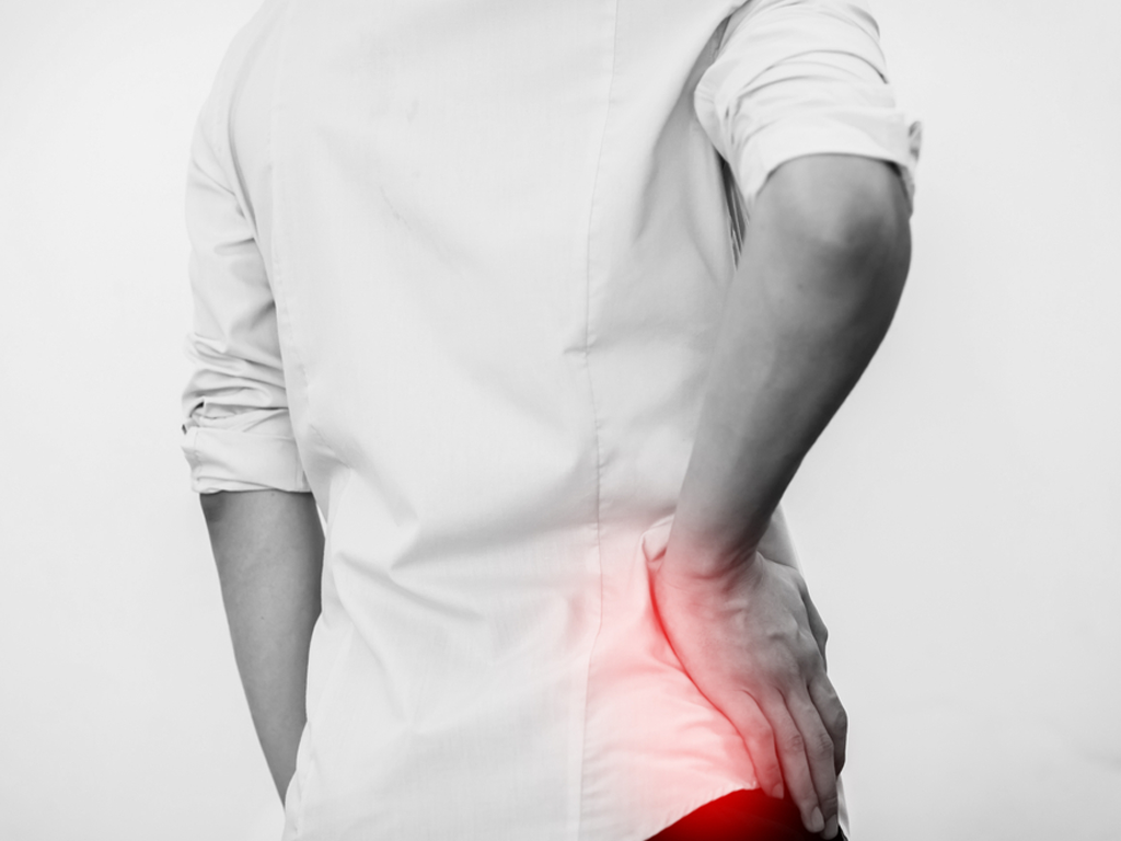 Person in white shirt holding their hip, with the hip area highlighted in red.