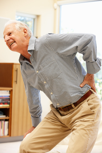 Older man grimacing while holding his lower back.