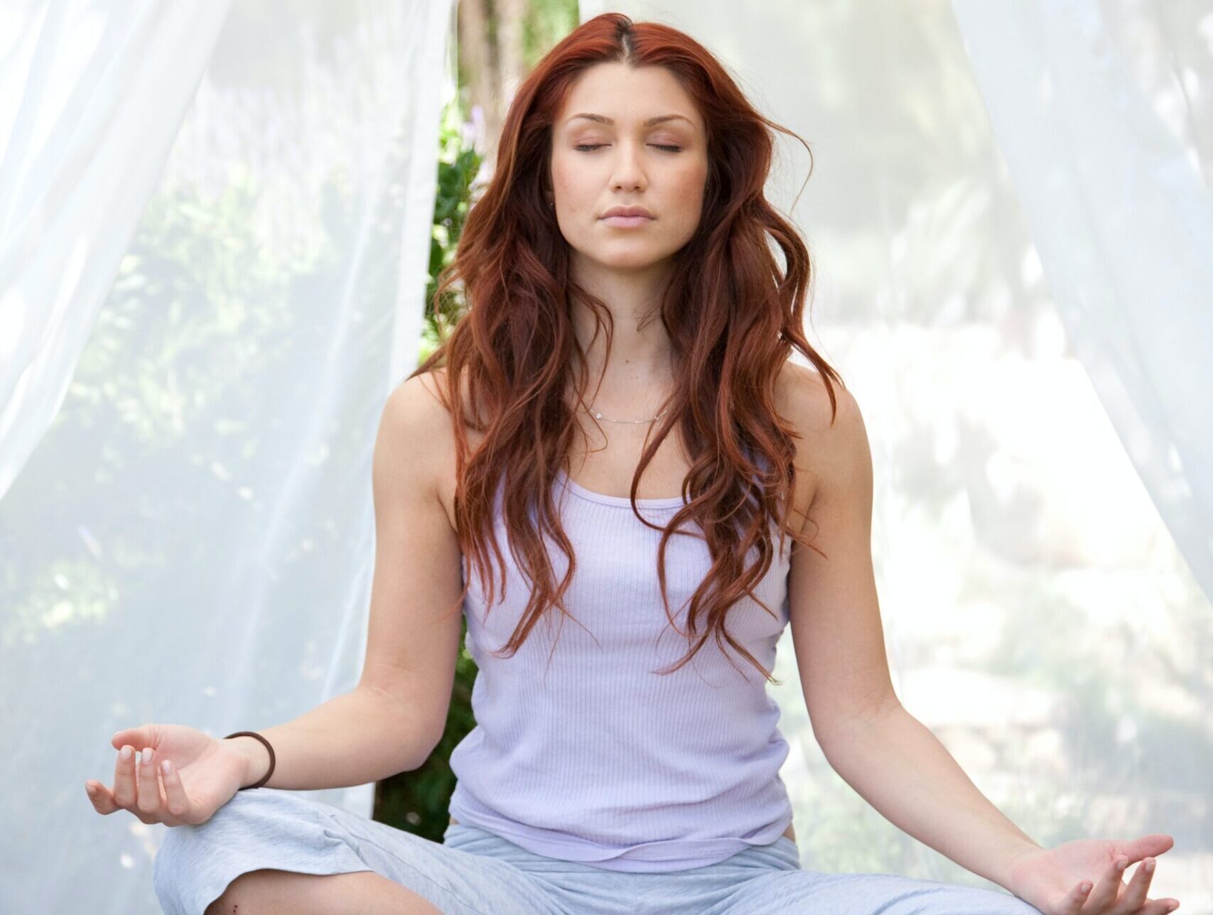 Red-haired woman sitting cross-legged with eyes closed and hands resting palms-up in a meditation pose