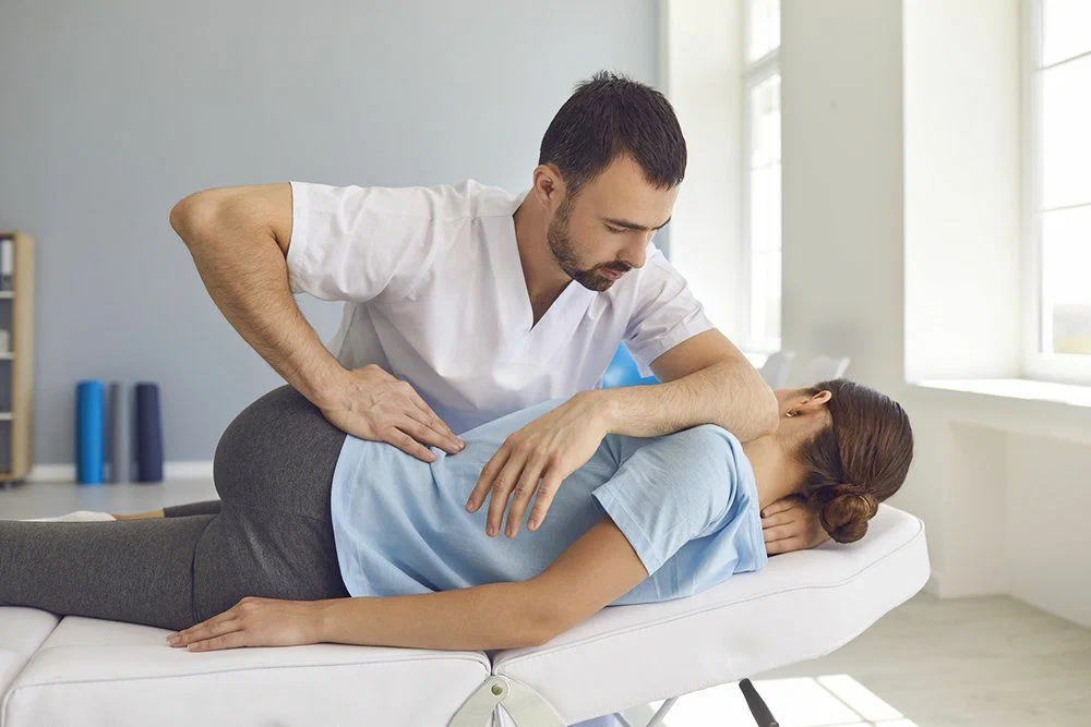 Practitioner performing a back adjustment on a woman lying on her side on a treatment table