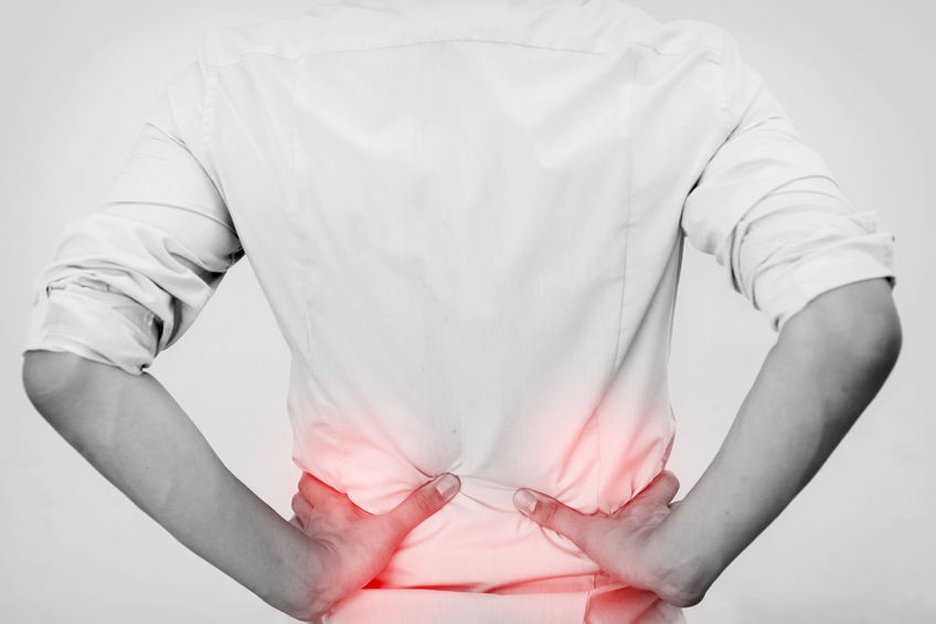 Person in a white shirt pressing both hands against their lower back, highlighted in red.