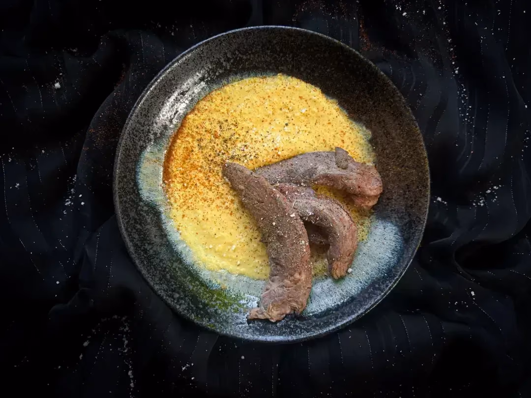 Dans un petit saladier en faïence de couleur bleu se trouve trois généreuses aiguillettes de canard déposées sur un lit de purée de maïs.