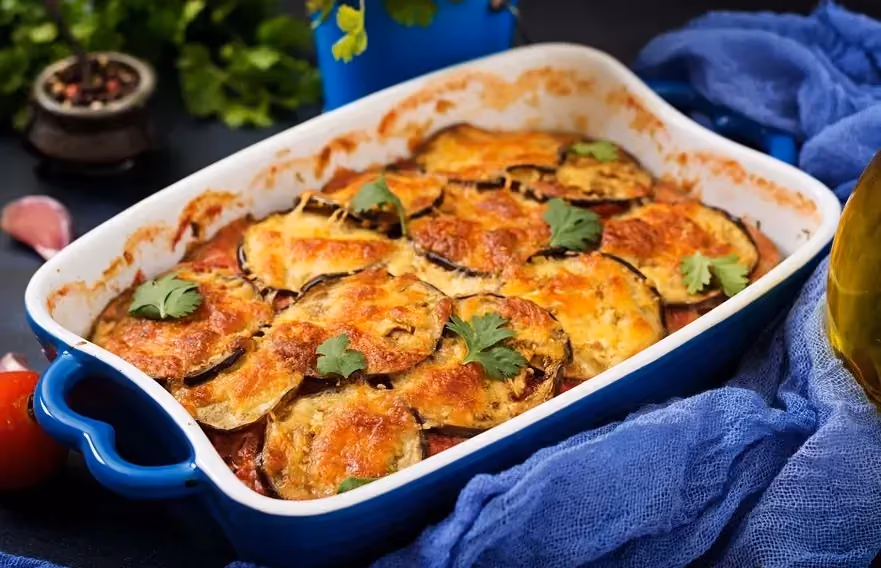 Dans un plat à gratin en faïence bleu se trouve les aubergines coupées en rondelles avec du parmesan. Elles recouvrent la viande de boeuf haché.