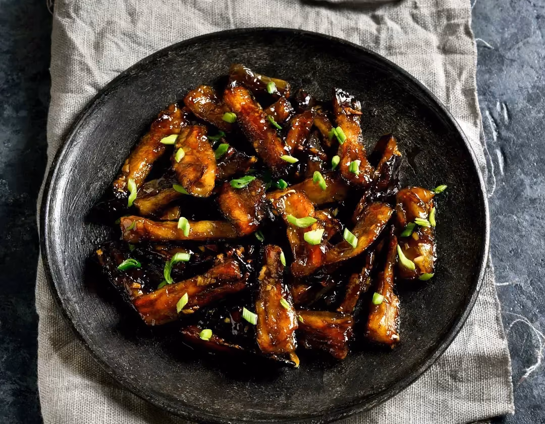 Dans une assiette plate de couleur noire. Les aubergines façon teriyaki sont parfaitement grillées et elles ont un aspect laquées.