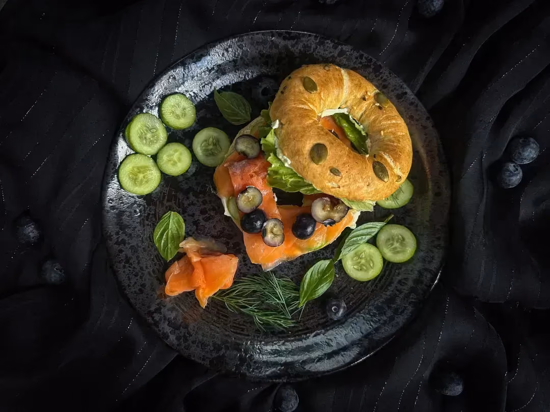 The salmon, cream cheese, and blueberry bagel is presented on a beautiful dark-colored plate.