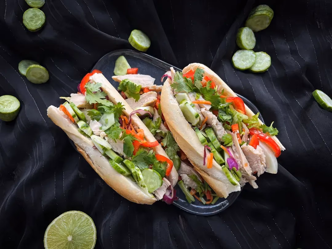 Inside an open half baguette, there is well-grilled chicken sliced thinly, with shredded carrots and finally some cilantro to finish.