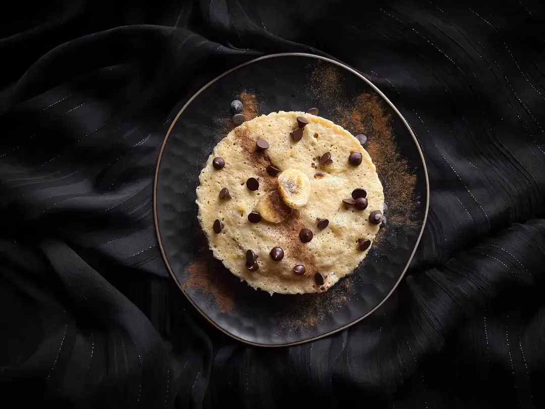 The protein banana bread is presented in a small bowl. The topping consists of two small banana slices and chocolate chips.