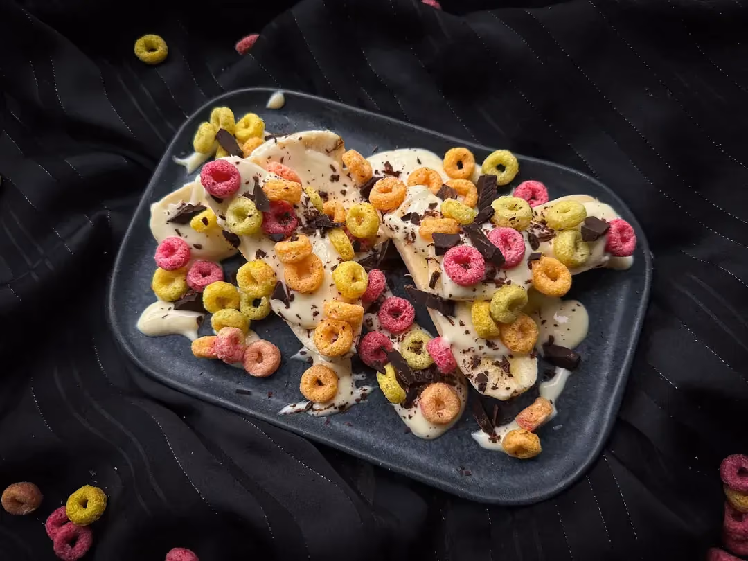 On a plate, there is a large banana cut in half lengthwise, served with raspberries, blackberries, and chocolate muesli.
