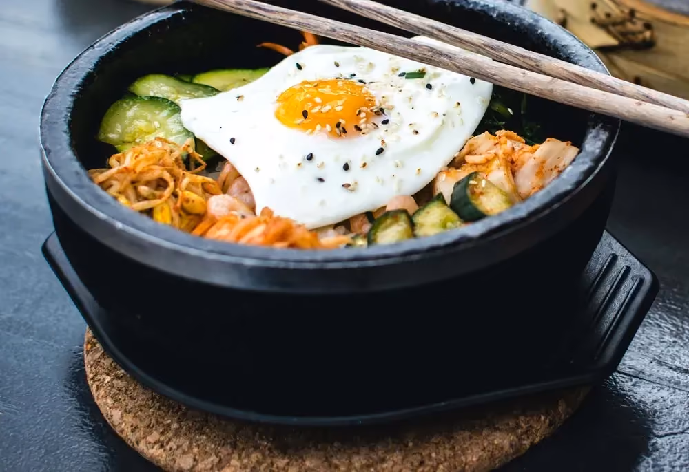 In a large cast-iron salad bowl, you can see all the ingredients that make up this bibimbap. A fried egg sits on top.