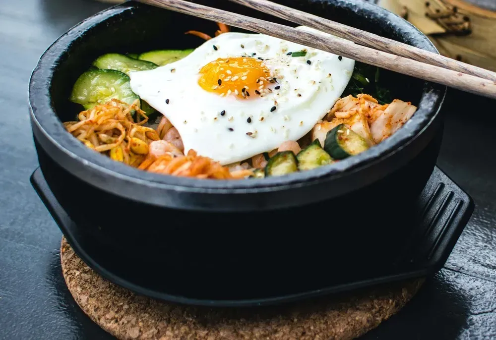 In a large cast-iron salad bowl, you can see all the ingredients that make up this bibimbap. A fried egg sits on top.