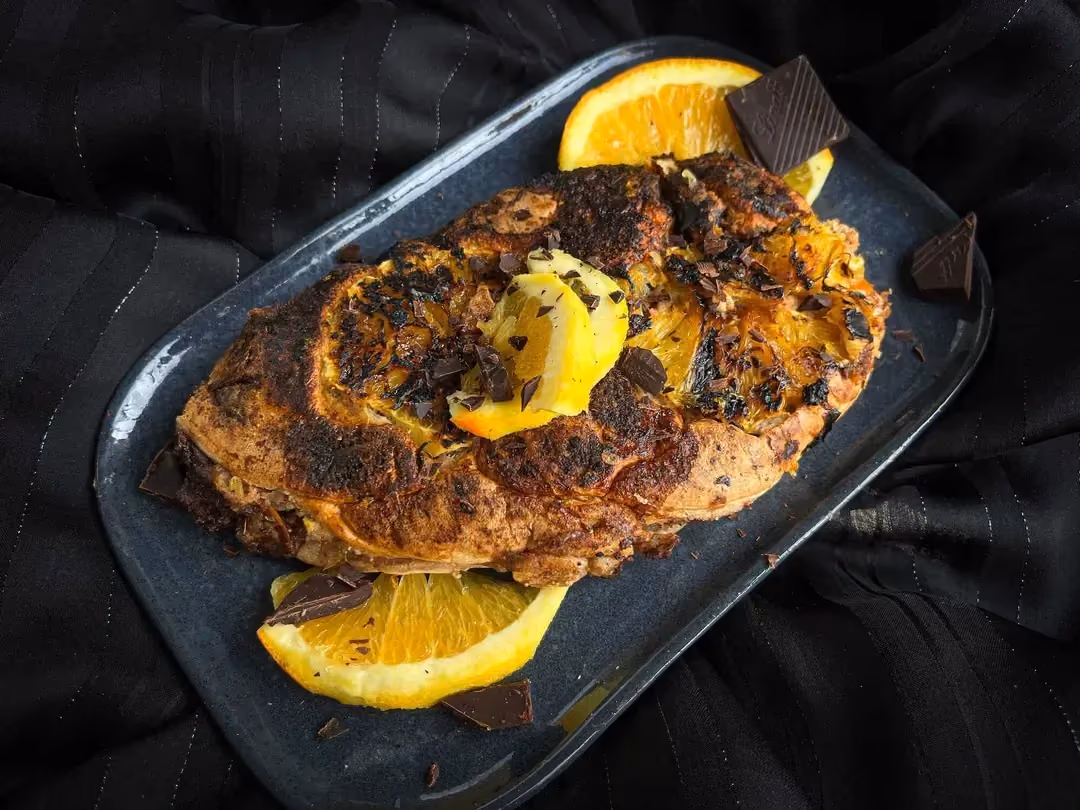 Served on a shallow rectangular plate, the orange, cinnamon, and chocolate big cake is accompanied by small lemon slices.