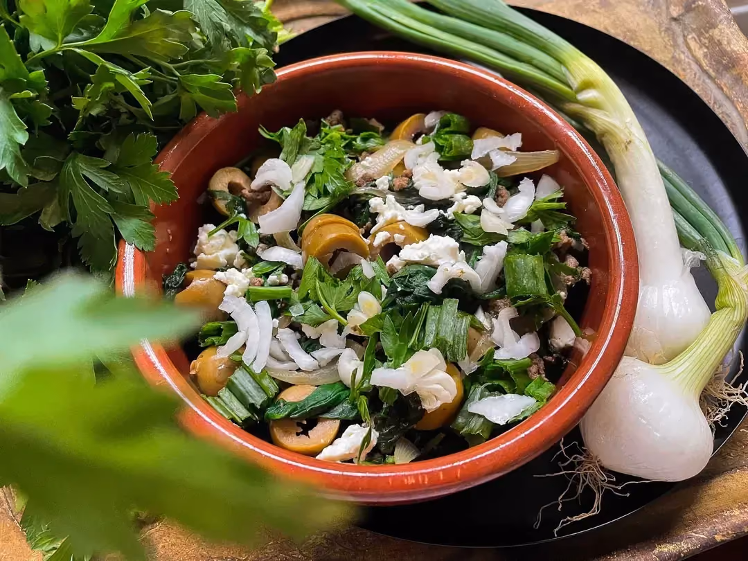 A terracotta mixing bowl holds the mixture of the recipe's different ingredients. Next to it are chives and two sweet onions.