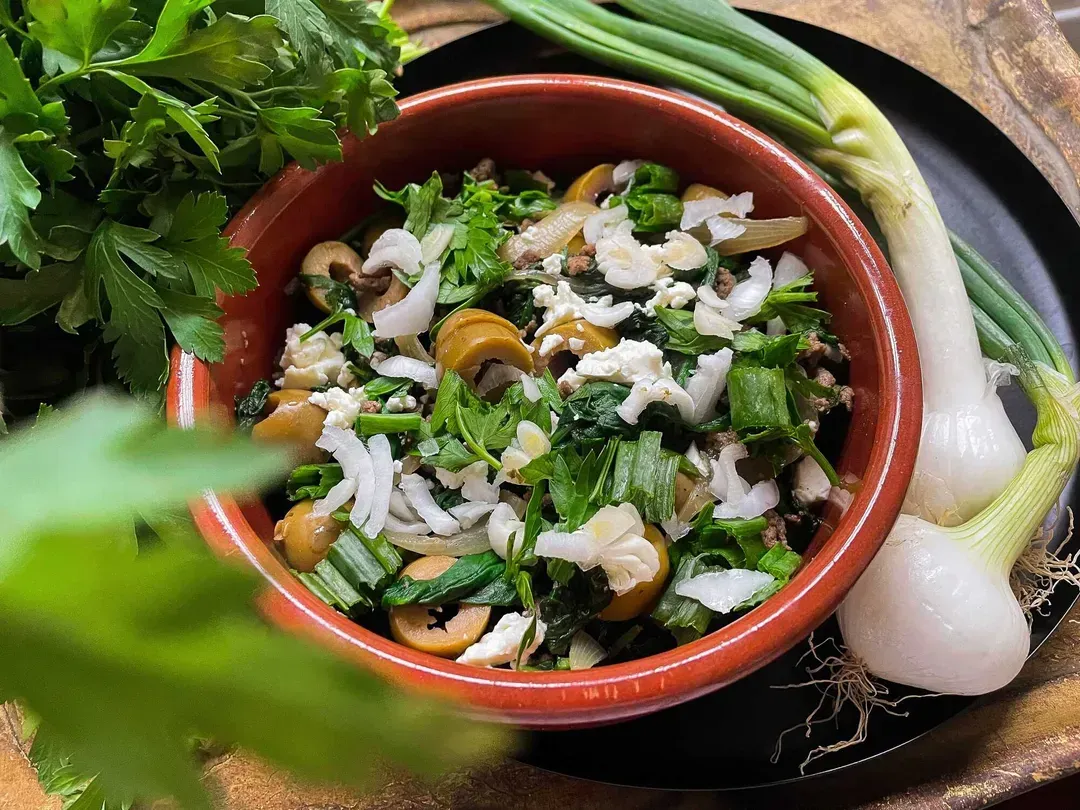 A terracotta mixing bowl holds the mixture of the recipe's different ingredients. Next to it are chives and two sweet onions.
