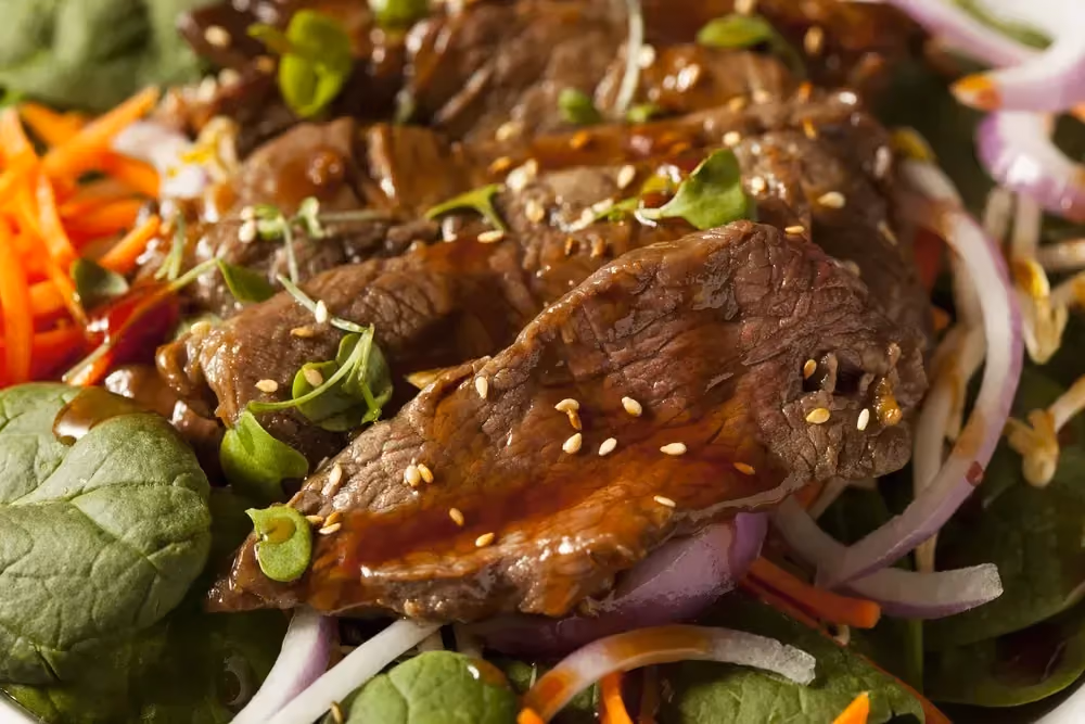 Dans un plat se trouve de belles tranches de faux-filet de boeuf. il est accompagné de carottes râpées et de pousses d'épinard.