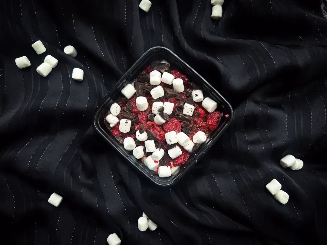 A small square earthenware dish is used to present the Weetabix bowl recipe with raspberries, marshmallows, and dark chocolate.