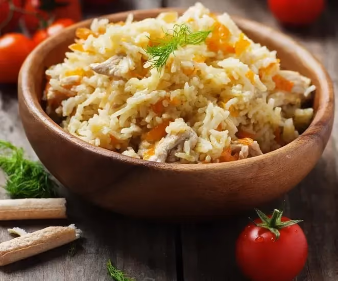 Dans un grand bol en terre cuite se trouve le riz pilaf et le poulet. Autour du plat quelques grosses tomates sont disposées.