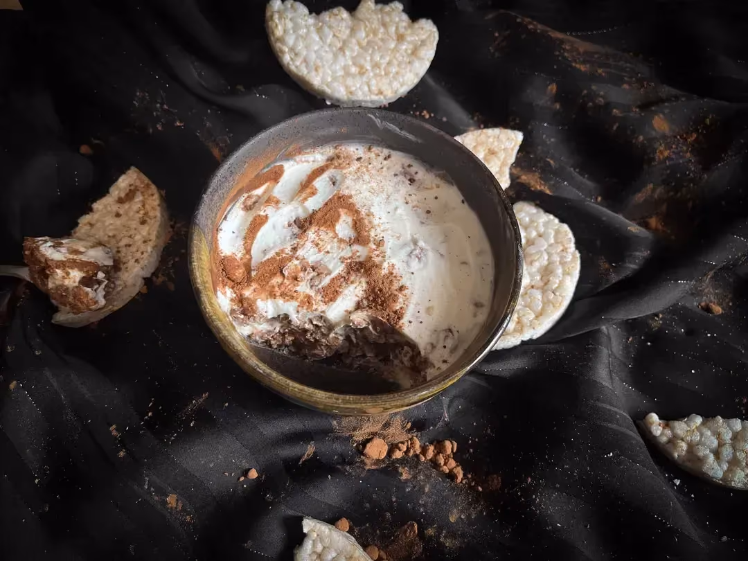 La recette de bol tirami riz choco peanut est présentée dans un bol en grès de couleur bleu. Des galettes de riz se trouvent à côté du plat.