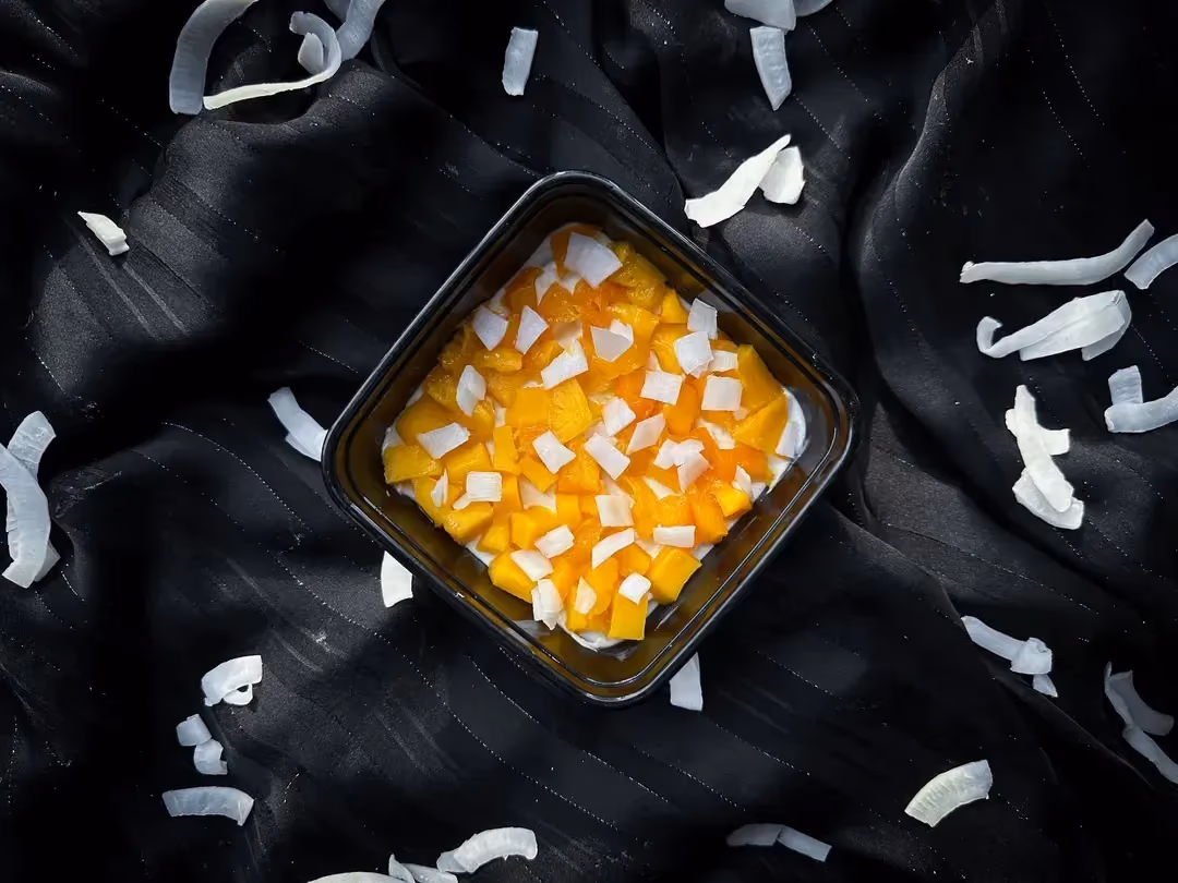 A pretty small square black earthenware dish holds thin coconut flakes and mango cut into small cubes.