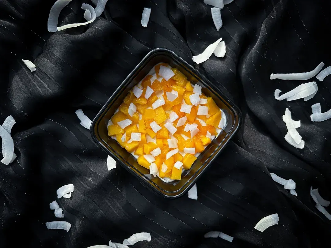 A pretty small square black earthenware dish holds thin coconut flakes and mango cut into small cubes.