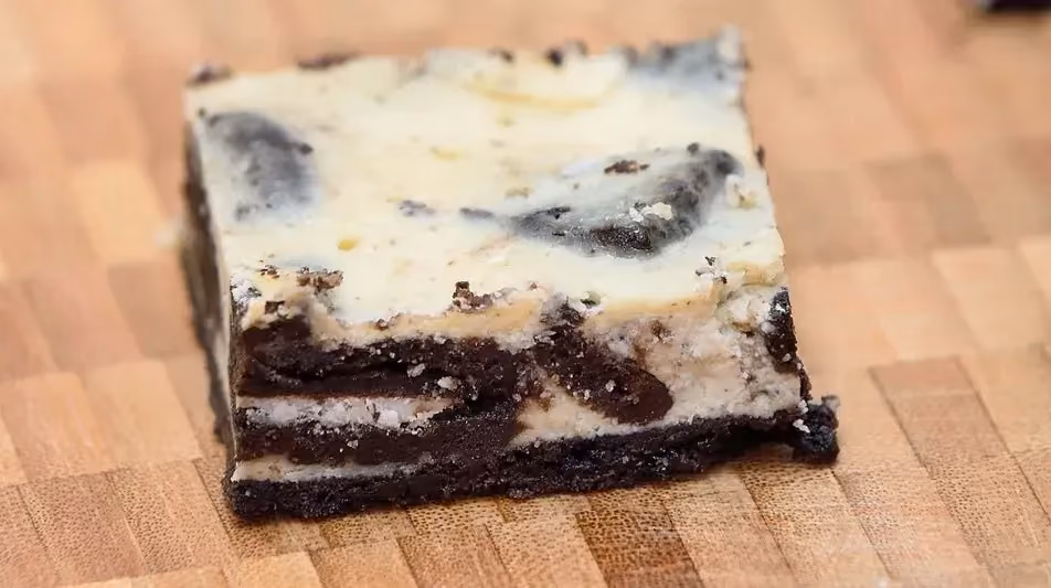 Sur un plan de travail en bois se trouve une grosse part de cheesecake Oréo avec du fromage blanc sur le dessus.